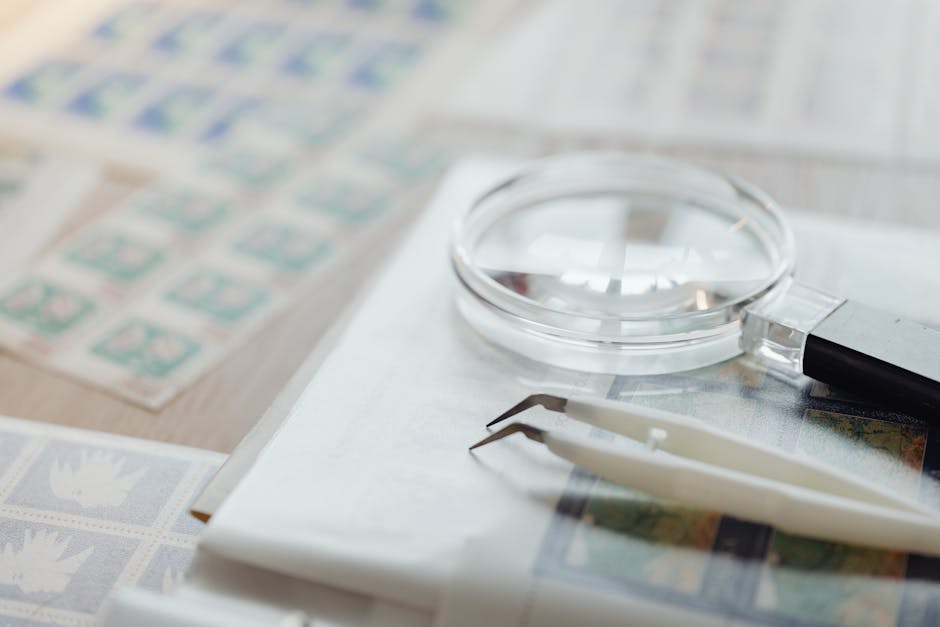 Magnifying glass and tweezers on a collection of postage stamps, ideal for philately enthusiasts.